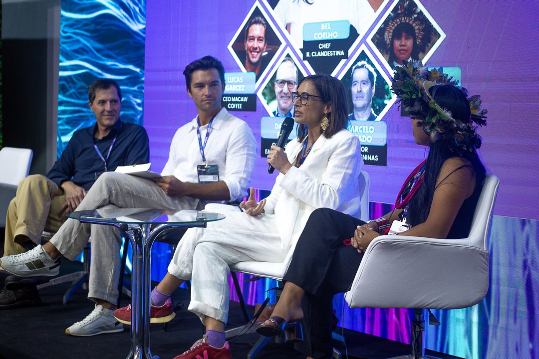 Bel Coelho speaking on the panel, with the full lineup on screen