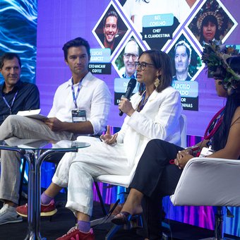 Bel Coelho speaking on the panel, with the full lineup on screen